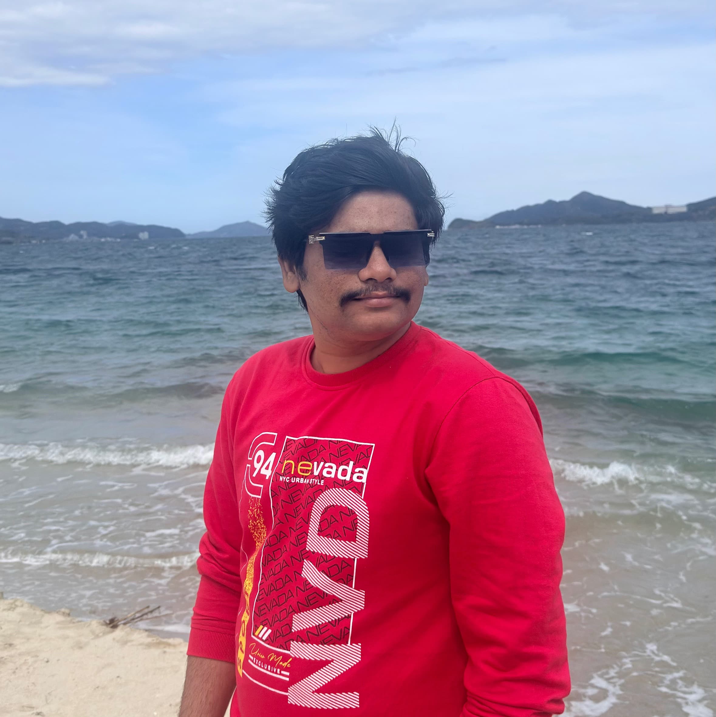 Yash Kadam standing on a beach, sea and hills behind him